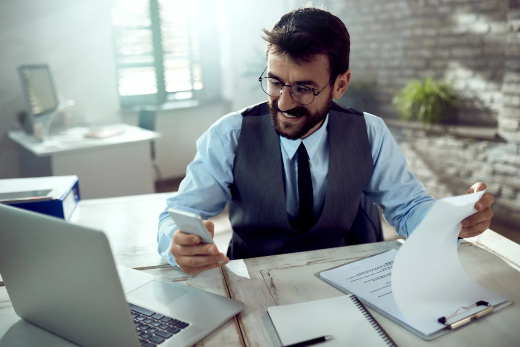 young happy businessman going through reports using smart phone office